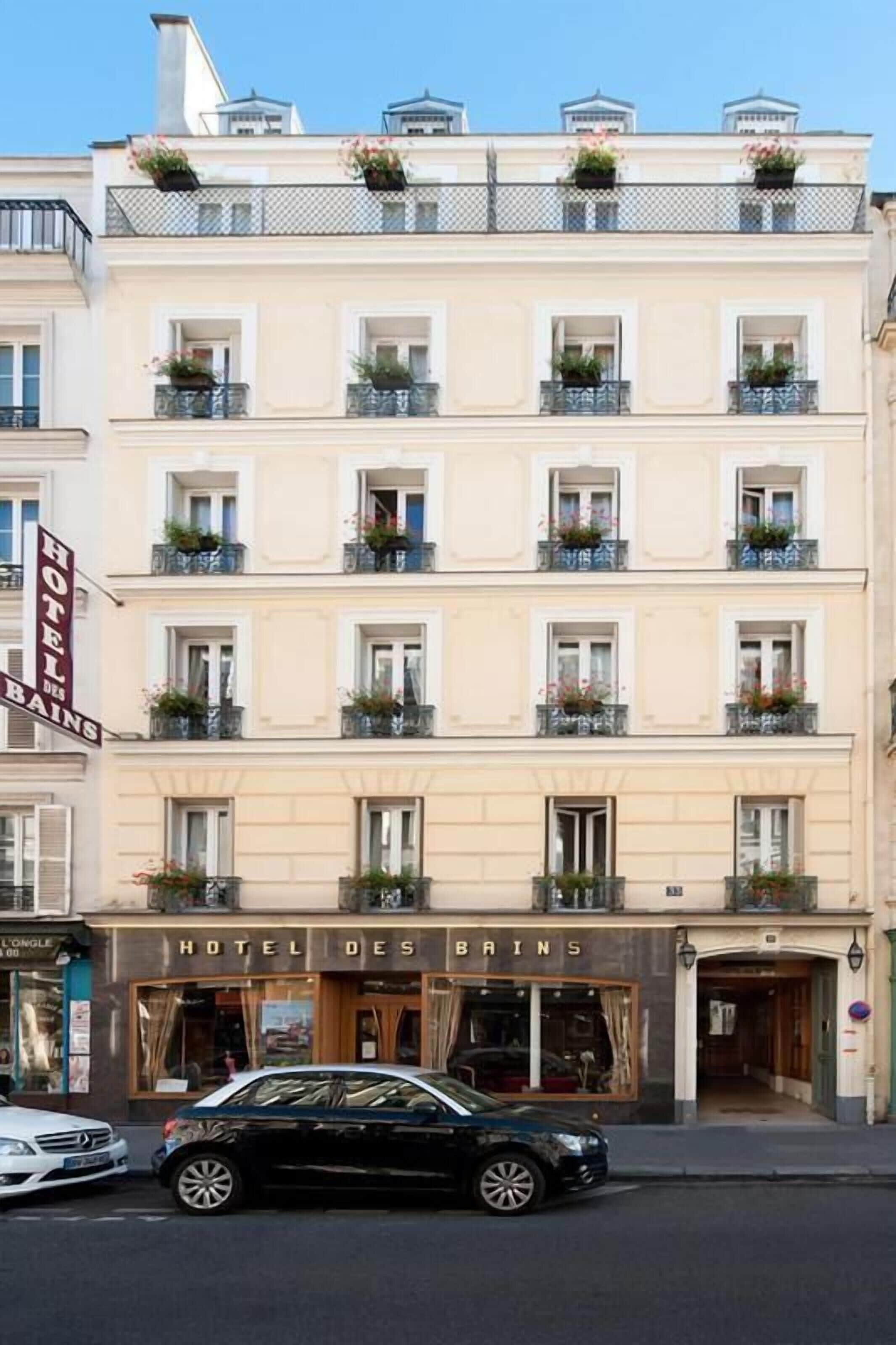 Un hotel de varios pisos con balcones, un coche estacionado frente a él y un letrero que dice "HOTEL DES BAINS".