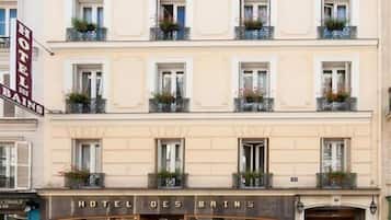 Un hotel de varios pisos con balcones, un coche estacionado frente a él y un letrero que dice "HOTEL DES BAINS".