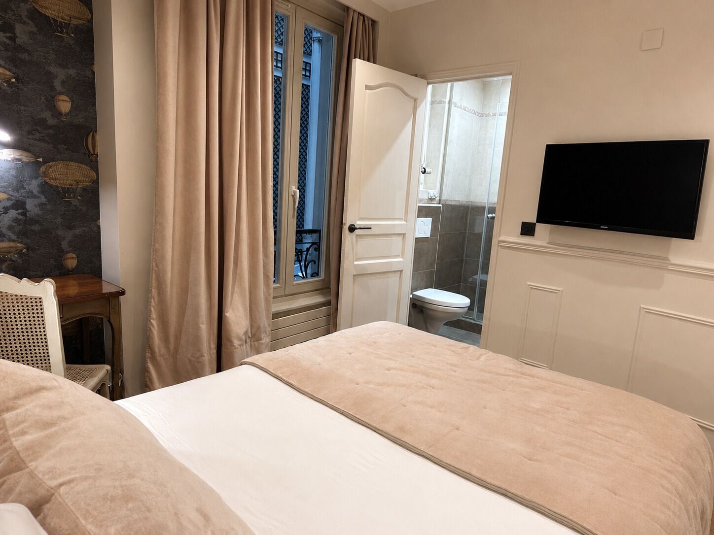 A bedroom with a bed, a television, a window with curtains, and a bathroom visible through the door.