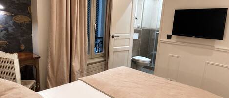 A bedroom with a bed, a television, a window with curtains, and a bathroom visible through the door.