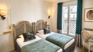 Et hotelværelse med to senge, en stol, et bord og et vindue med gardiner.