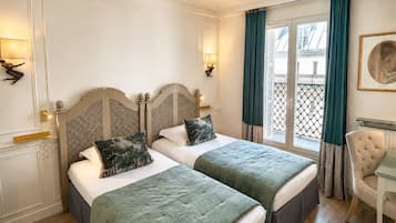 Habitación de hotel con dos camas, una silla, una mesa y una ventana con cortinas.