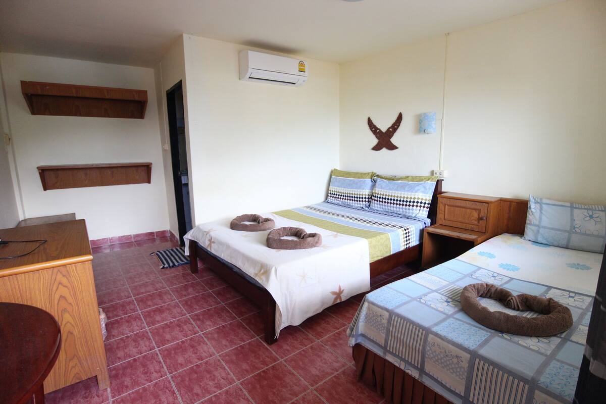 A bedroom with a bed, a desk, and a chair. There is an air conditioning unit on the wall.