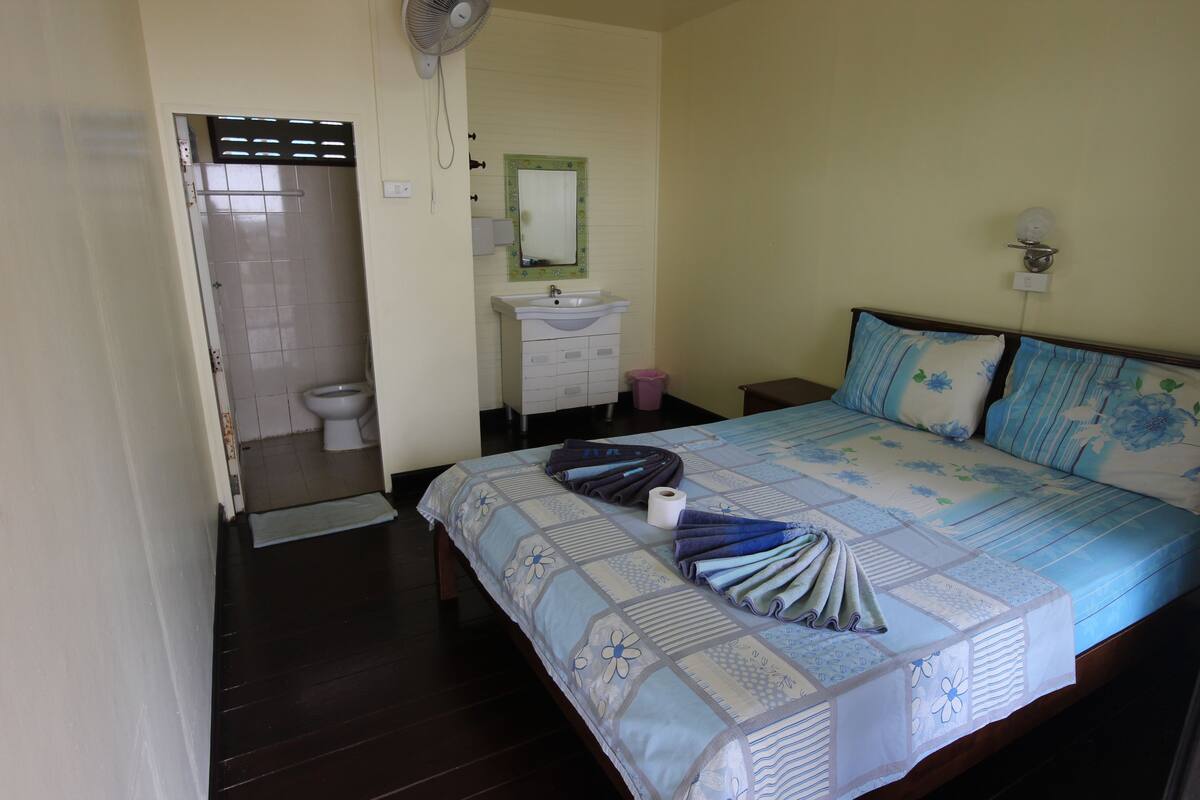 A bedroom with a bed, a bedside table, a nightstand, a mirror, a window, and a door leading to a bathroom.