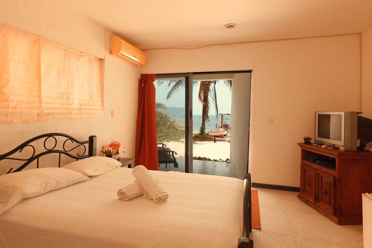 A hotel room with a bed, a television, and a view of the beach through the door.