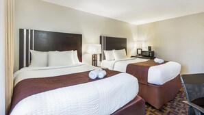 Een hotelkamer met twee bedden, een bureau, een stoel, een magnetron en een lamp.
