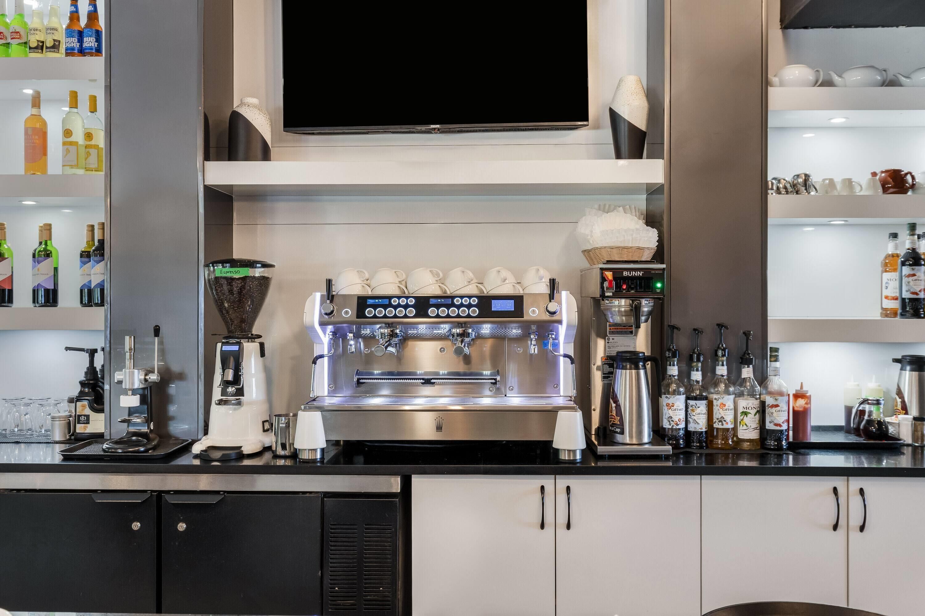 A bar area with a coffee machine, shelves with bottles, and a television above.