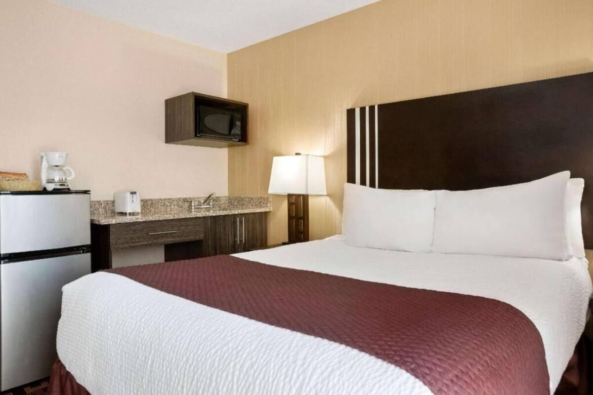 Ein Hotelzimmer mit einem Bett, einer Mikrowelle, einer Kaffeemaschine, einer Lampe und einer kleinen Küchenzeile.