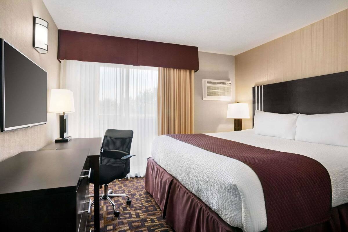 Ein Hotelzimmer mit Bett, Schreibtisch, Stuhl, Fernseher und einem Fenster mit Vorhängen.