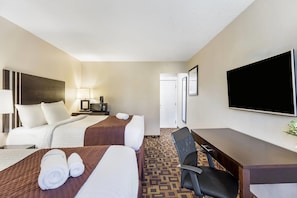 A hotel room with two beds, a desk, a chair, a television, and a door.