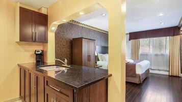 A hotel room with a kitchenette, a bed, and a bathroom.