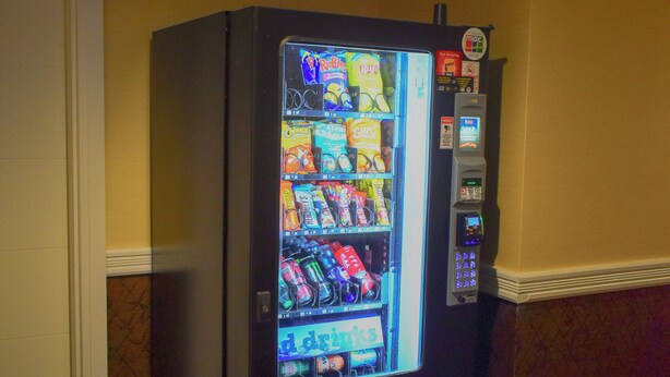 A vending machine in a room with patterned carpet and yellow walls. - Days Inn by Wyndham Sylvan Lake (Sylvan Lake)