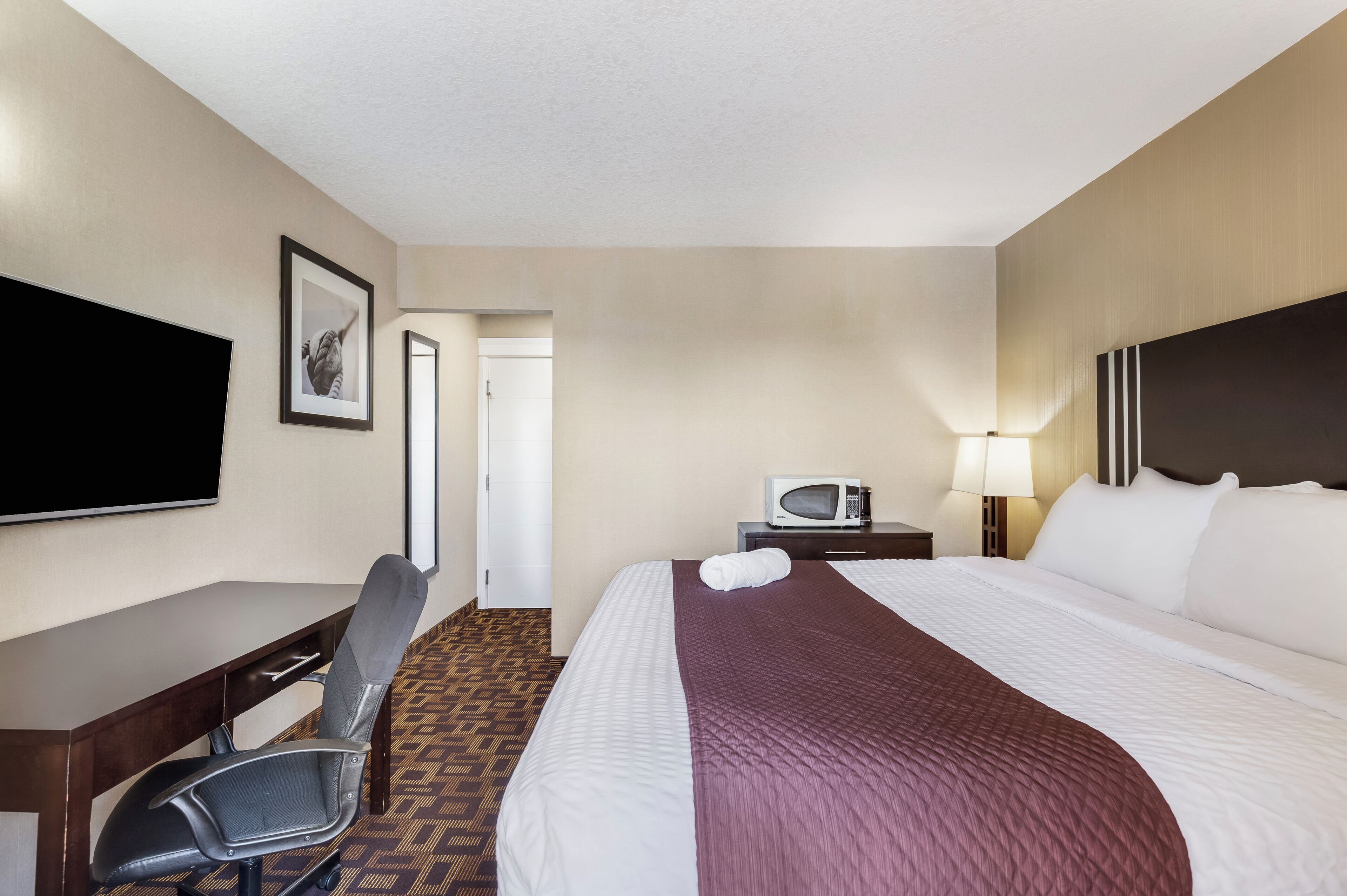 A hotel room with a bed, a desk, a chair, a television, a microwave, and a door.