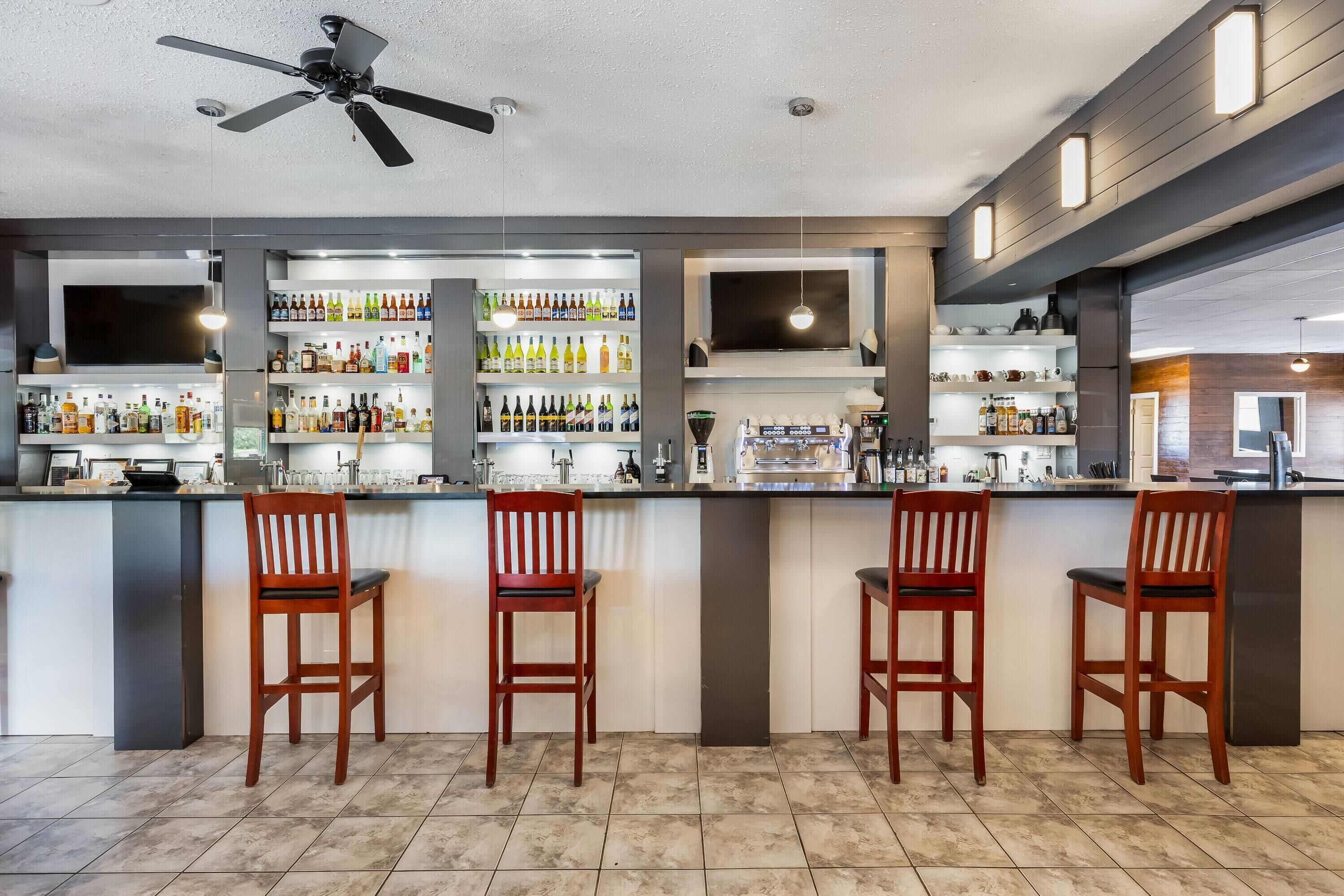 A bar area with a ceiling fan, shelves of bottles, and bar stools.