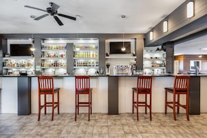 Zona de bar con ventilador de techo, estantes con botellas y taburetes.