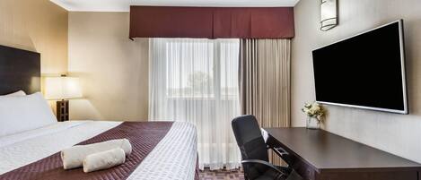 Habitación de hotel con cama, escritorio, silla, televisión y ventana con cortinas.