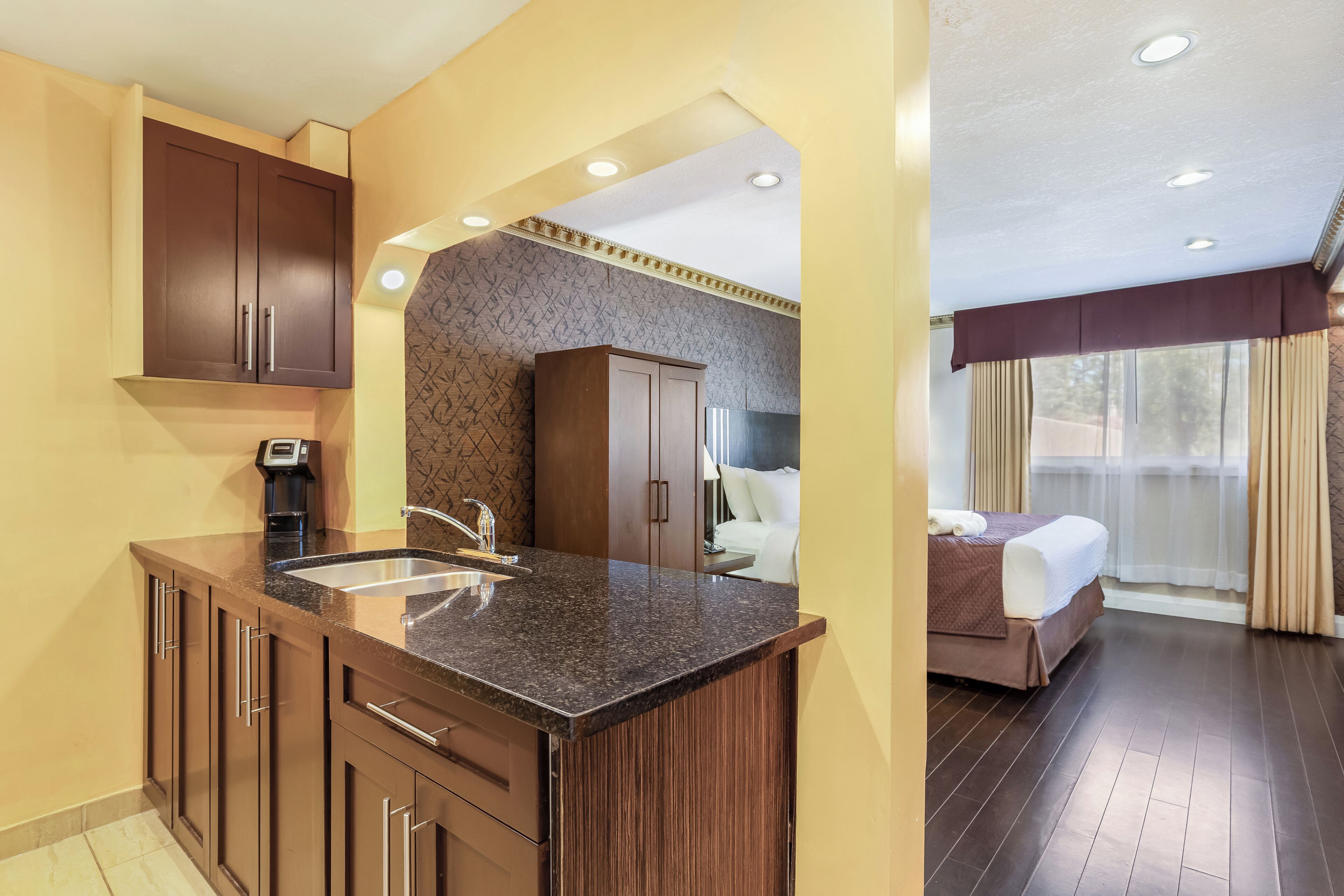 A hotel room with a kitchenette, a bed, and a bathroom.