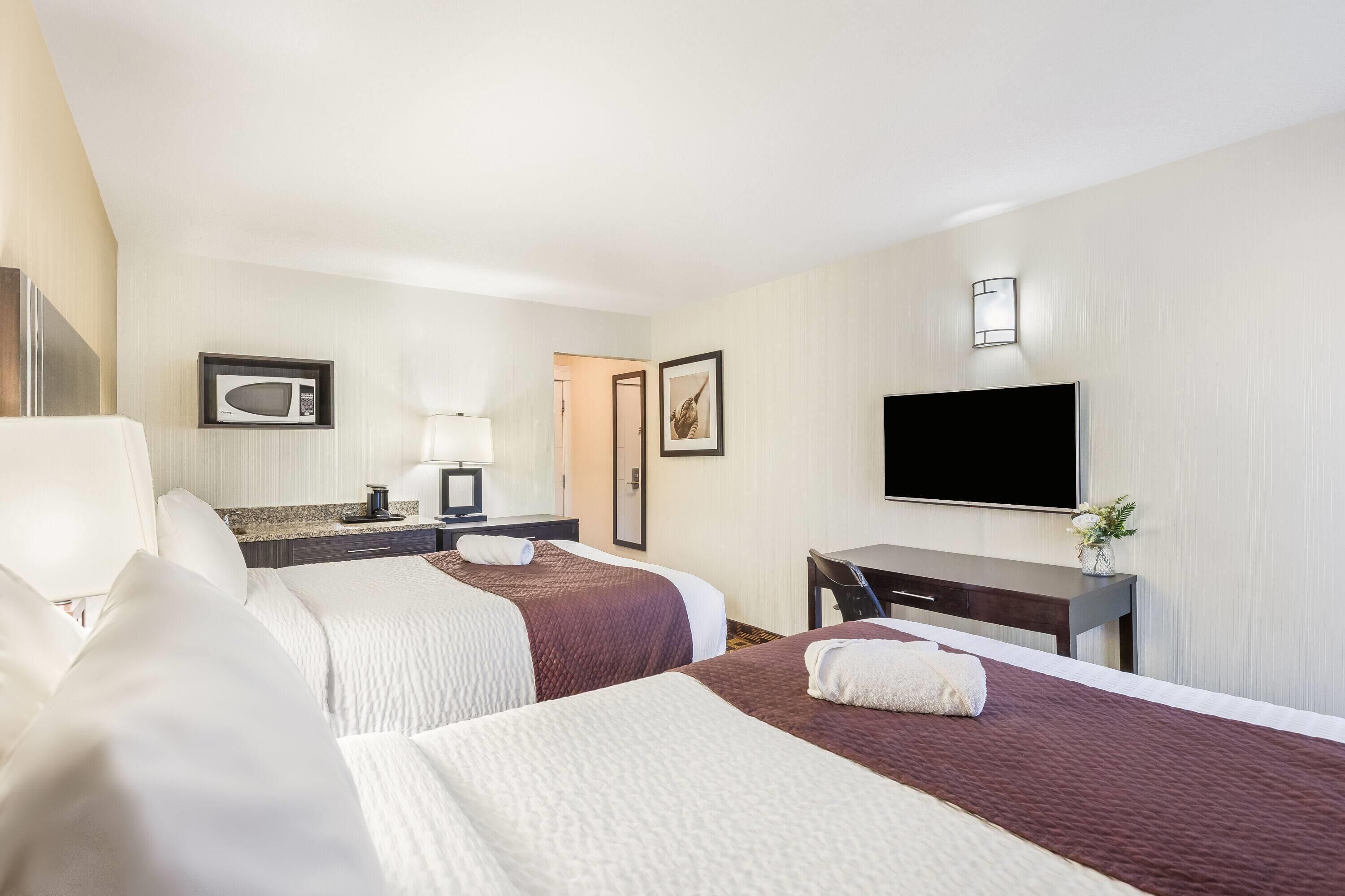 A hotel room with two beds, a desk, a television, a microwave, and a door.
