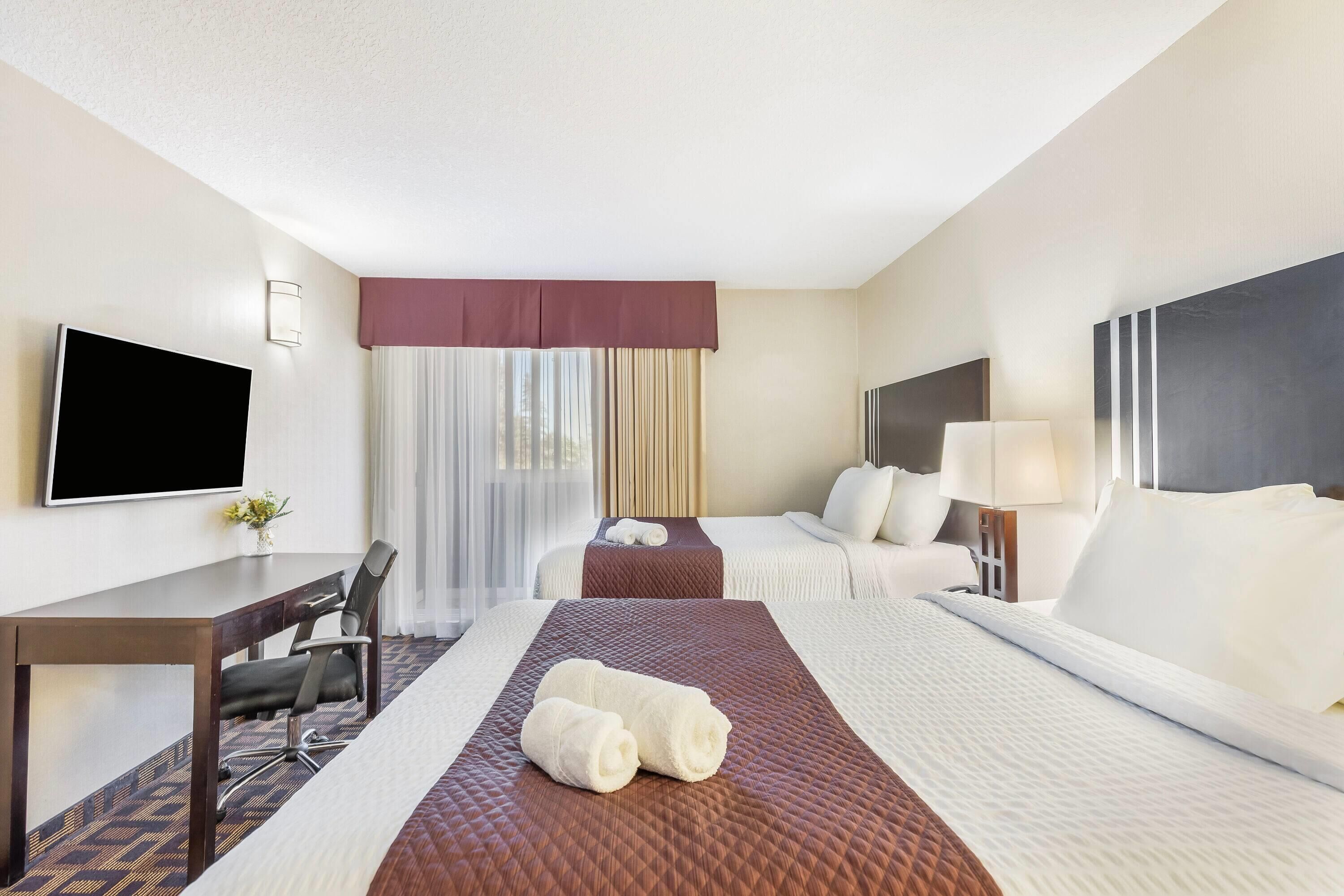 A hotel room with a bed, a desk, a chair, a TV, and a window with curtains.