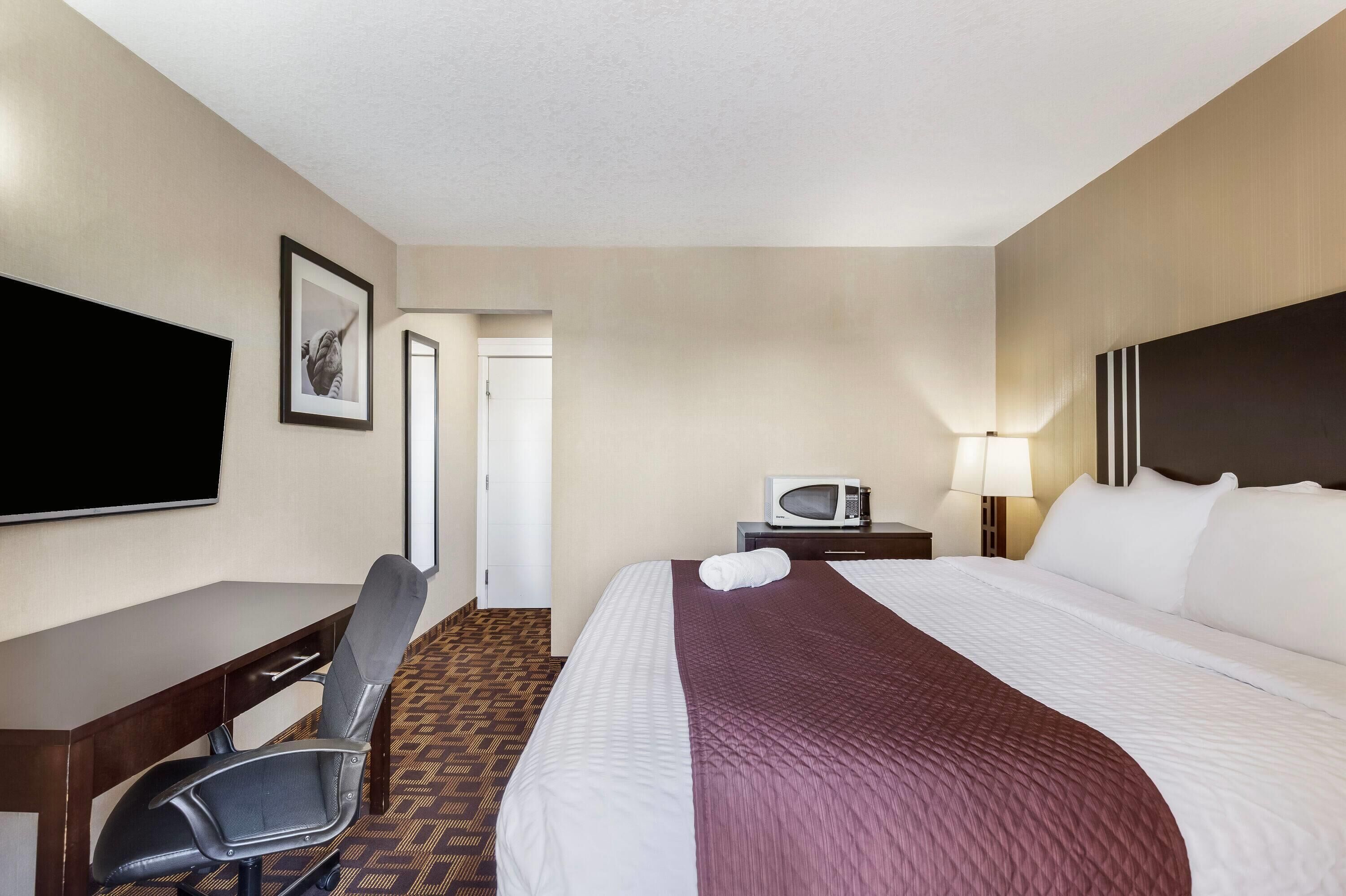 A hotel room with a bed, a desk, a chair, a television, a microwave, and a door.