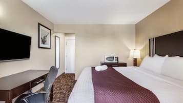 Quarto de hotel com uma cama, escrivaninha, cadeira, televisão, micro-ondas e porta.
