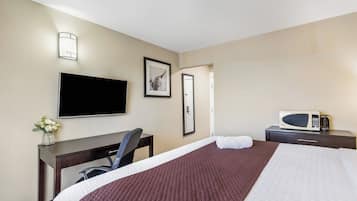 A hotel room with a bed, a desk, a chair, a television, a framed picture, and a microwave.