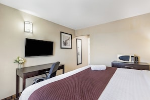 Une chambre d’hôtel équipée d’un lit, d’un bureau, d’une chaise, d’une télévision, d’un tableau encadré et d’un four à micro-ondes.