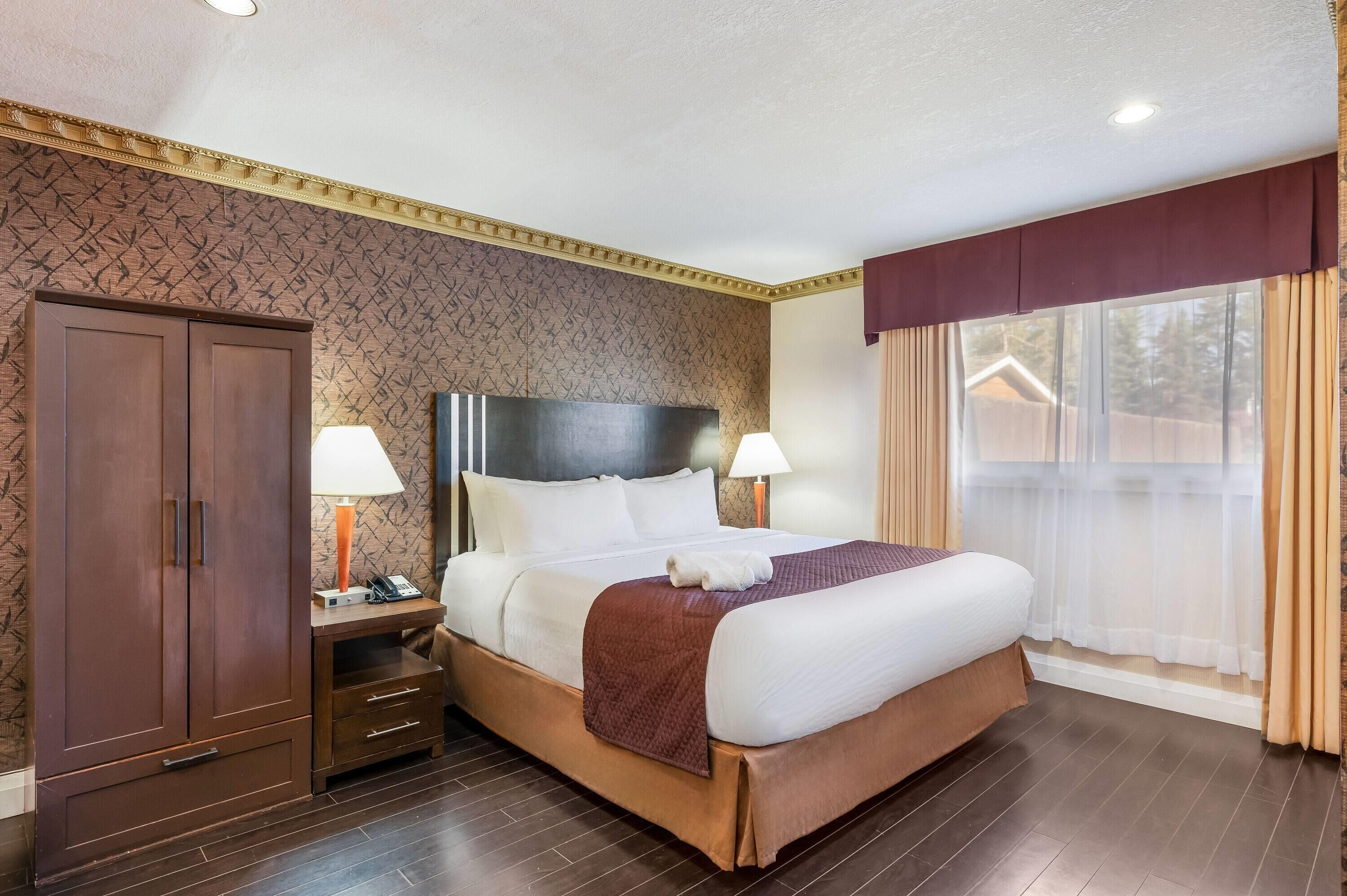 Une chambre d’hôtel avec un lit, des lampes de chevet, une armoire et une fenêtre avec des rideaux.