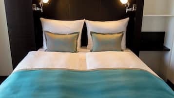 Una cama bien hecha con una colcha azul turquesa y blanca, dos almohadas a juego y lámparas de lectura fijadas en la pared.