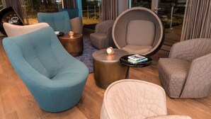 A modern living room with a teal armchair, a round black coffee table, and a large round chair with a quilted backrest. - Motel One München-Olympia Gate (Munich)