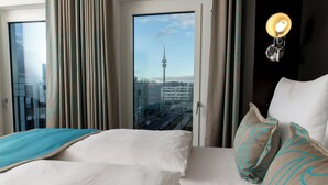 A hotel room with a large bed, a view of a tower, and a cityscape. - Motel One München-Olympia Gate (Munich)