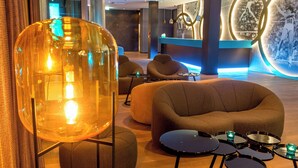 A modern lobby with a large transparent light fixture, comfortable seating, and a reception desk with a digital display. - Motel One München-Olympia Gate (Munich)