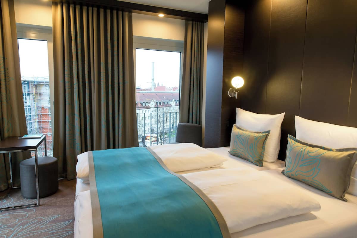 Ein Hotelzimmer mit einem großen Bett, einem Schreibtisch und Blick auf die Stadt durch das Fenster.