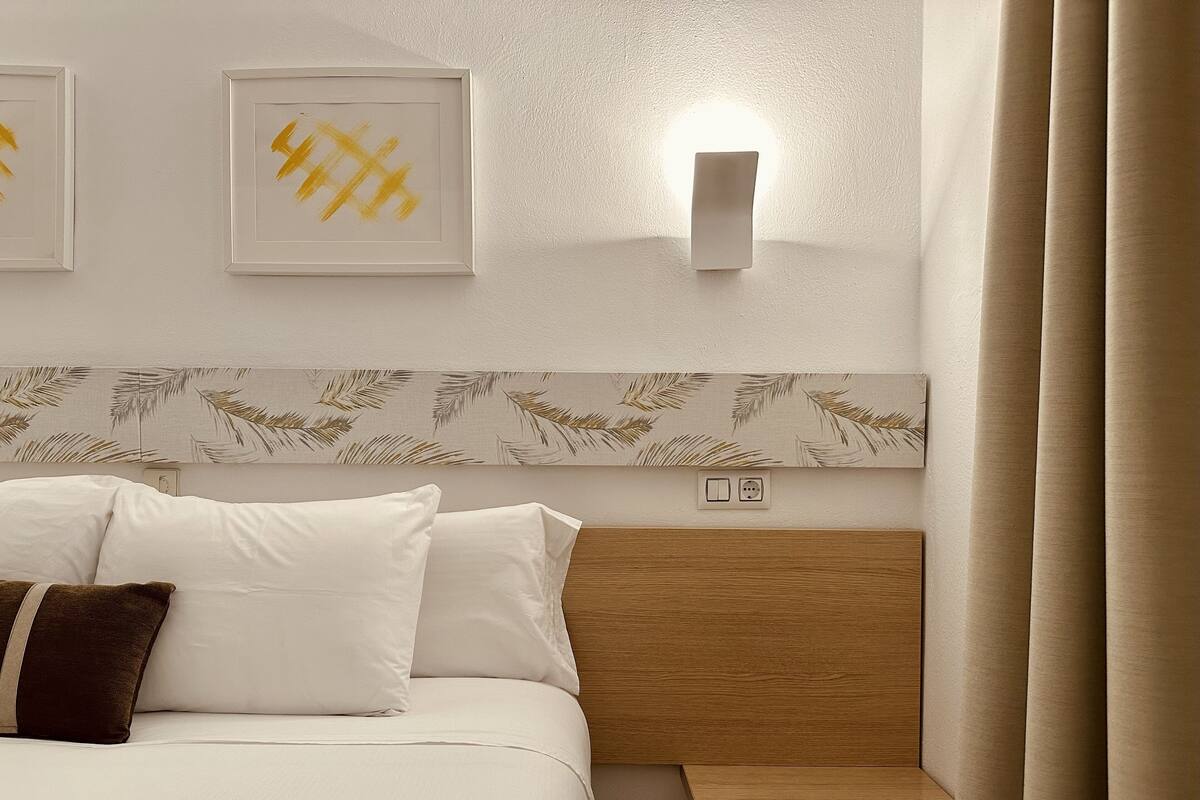 A neatly made bed with white and brown pillows, a wooden headboard, and a wall-mounted light fixture.