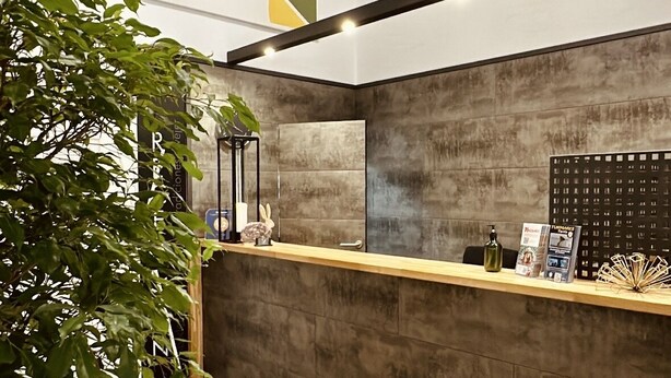 A reception area with a modern design, featuring a concrete reception desk, a clock on the wall, and a geometric wall decoration. - LUZ Vejer Hospedería (Vejer de la Frontera)
