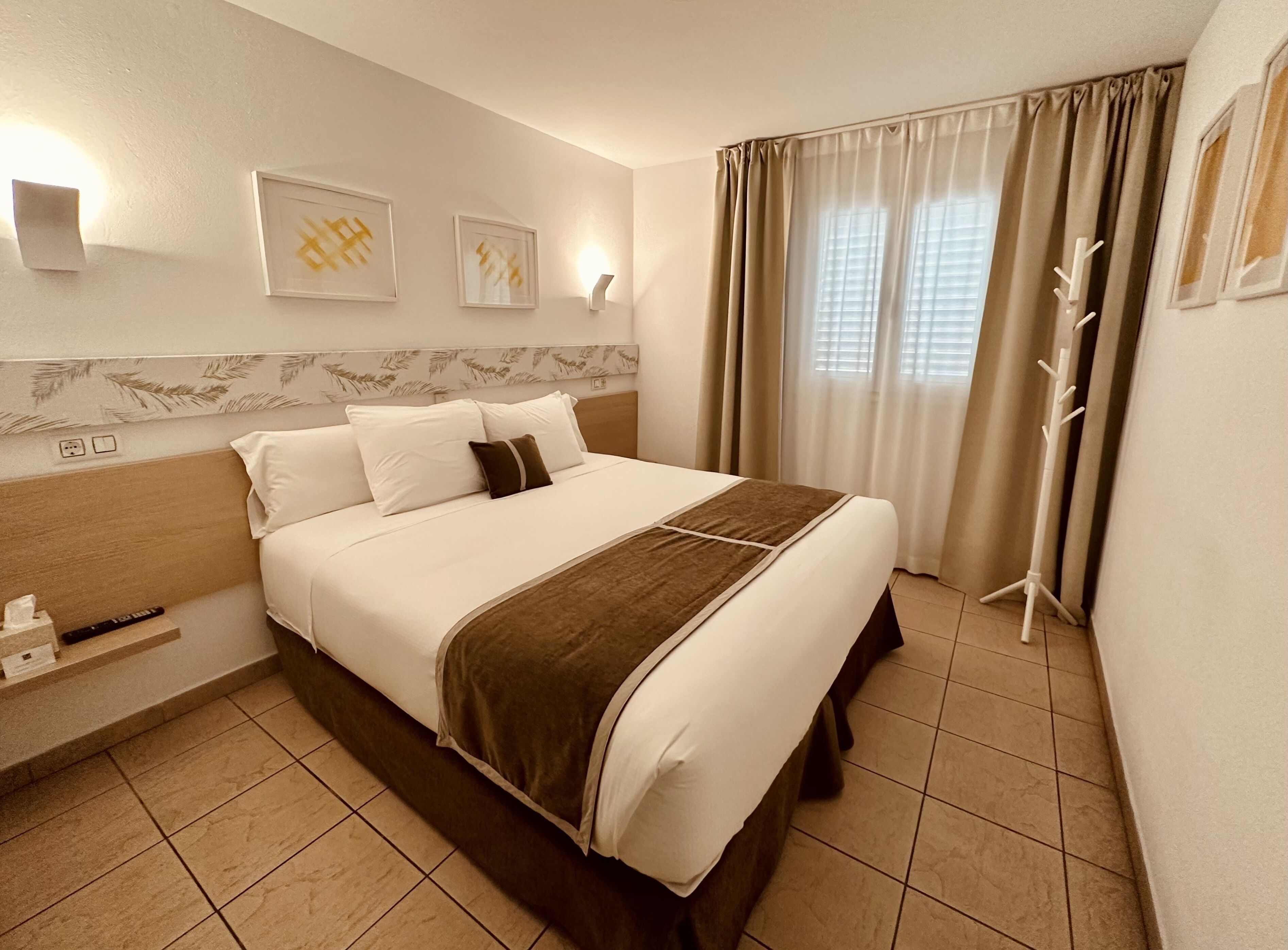 Una habitación de hotel con una cama, una mesita de noche, una lámpara y una ventana con cortinas.
