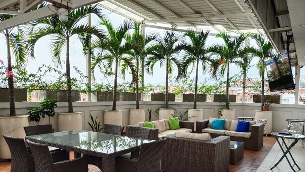 An outdoor patio area with wicker furniture, a glass table, and potted plants. - Apartasuites San Marcos (Cali)