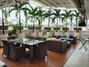 Un patio al aire libre con mobiliario de mimbre, una mesa de vidrio y plantas en macetas.