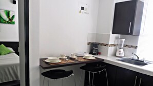 A compact kitchenette with a single sink, a coffee maker, and two bar stools. - Apartasuites San Marcos (Cali)