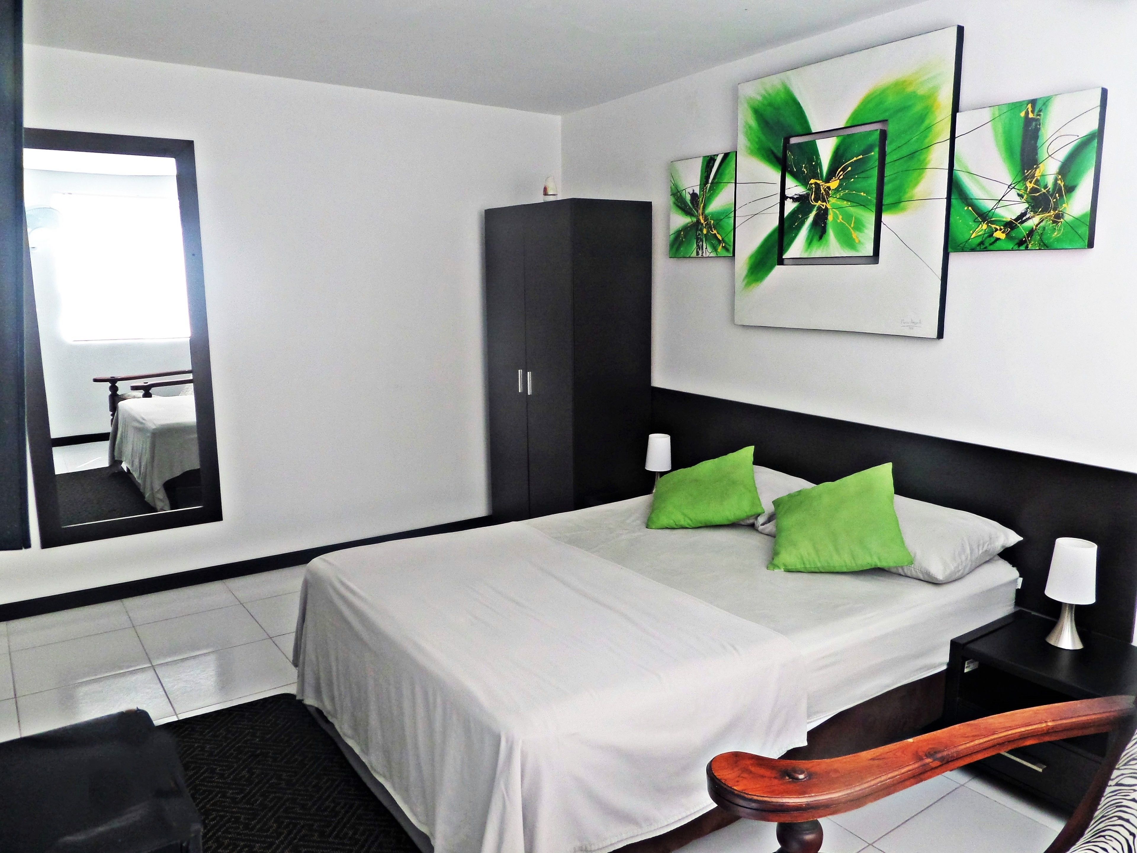 A hotel room with a bed, a wardrobe, a nightstand, and a mirror.