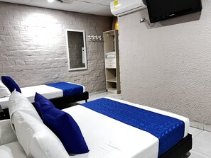 Hotellihuone, jossa on kaksi sänkyä, ja molemmissa on valkoiset ja siniset vuodevaatteet. Huoneessa on myös vaatekaappi, peili ja seinälle asennettu televisio.