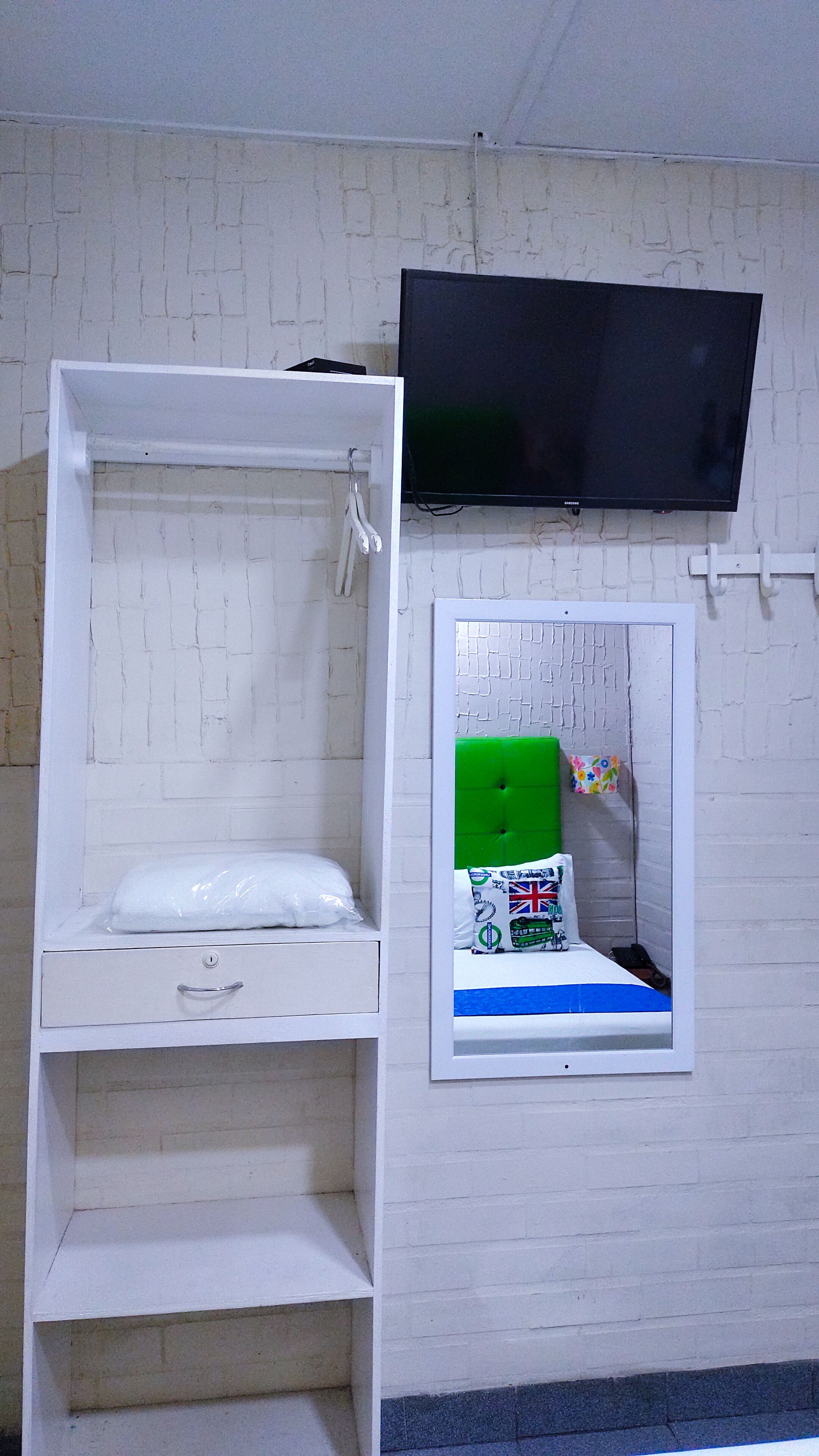 A bunk bed with a TV above it, a small window with a mirror, and a white wall with a brick pattern.