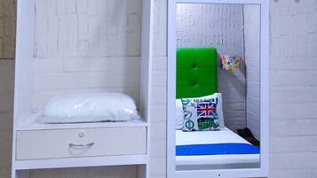 A bunk bed with a TV above it, a small window with a mirror, and a white wall with a brick pattern.