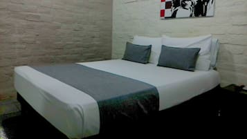 A single bed with a white and gray bedspread, two pillows, and a black and white abstract painting on the wall.