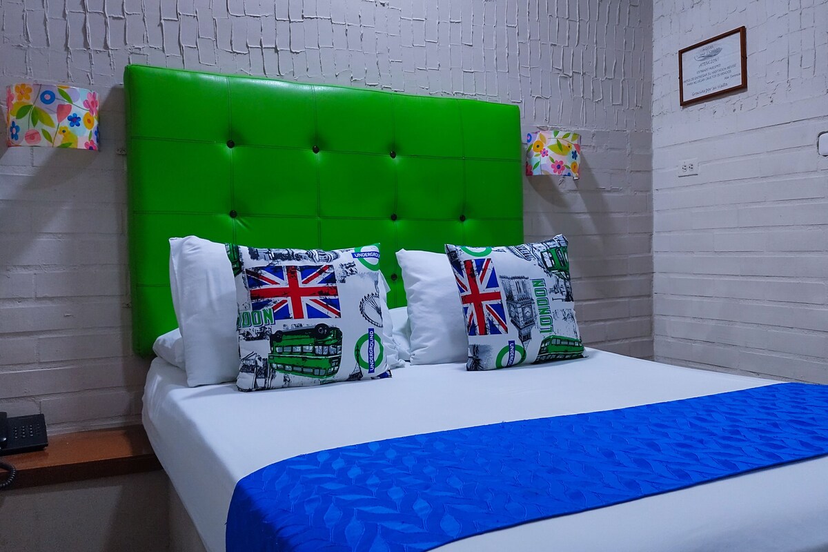 A bed with a green headboard, two pillows with London-themed designs, and a blue bedspread.