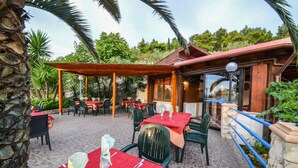 An outdoor dining area with tables set for two, surrounded by stone walls and palm trees. - Hotel Piccolo Paradiso (Peschici)