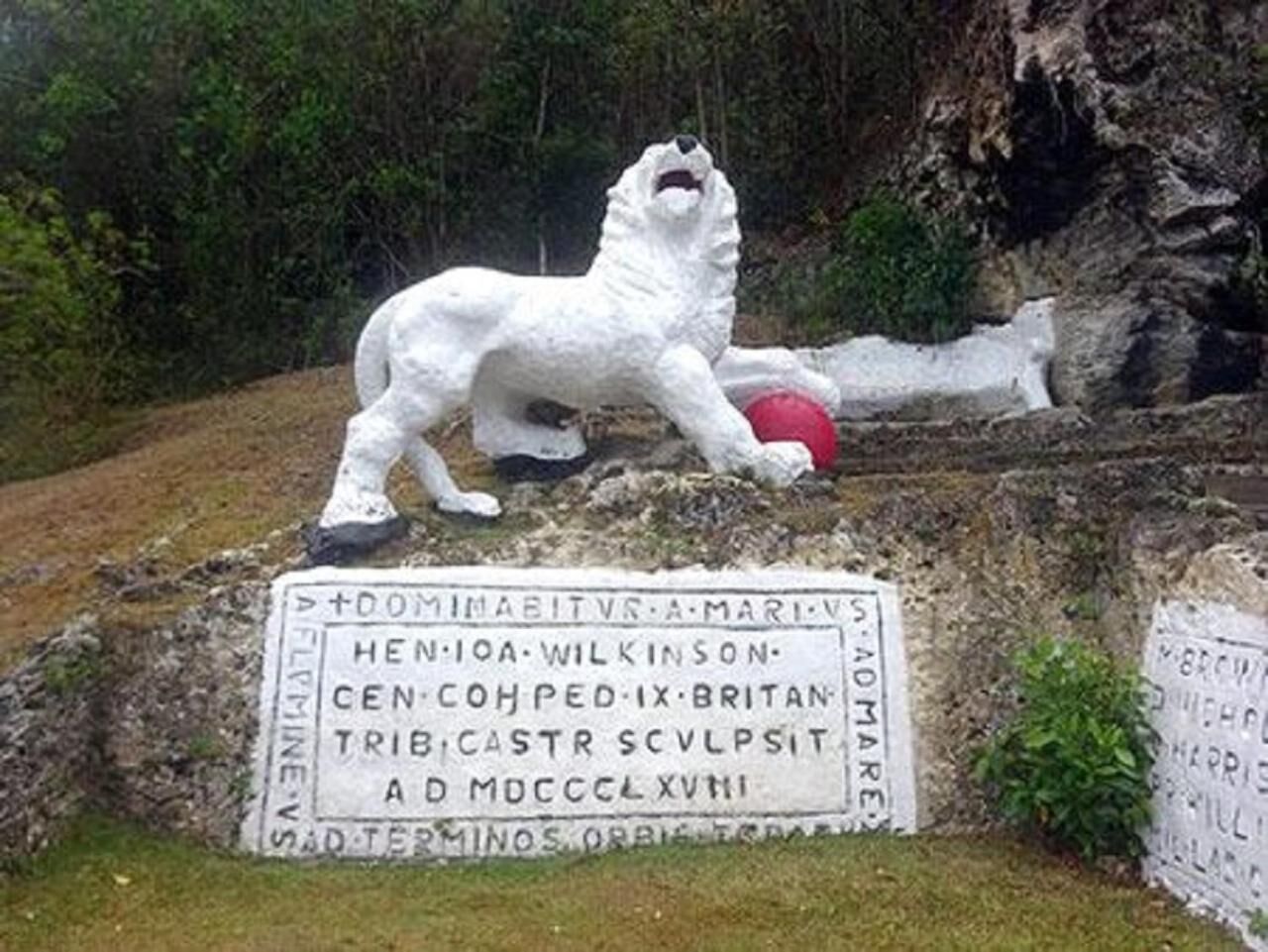 Una estatua blanca de piedra de un león con una esfera roja, rodeada de antiguas inscripciones.