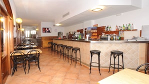 A restaurant with a bar area, multiple tables and chairs, and a tiled floor. - Hostal Montaña (Sant Antoni de Portmany)