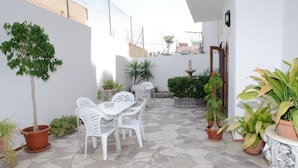 A patio with a white table and chairs, surrounded by potted plants and a stone floor. - Hostal Montaña (Sant Antoni de Portmany)