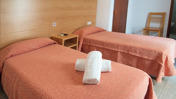 A hotel room with two beds, each covered with a textured orange blanket, and a neatly folded white towel on the bed in the foreground. - Hostal Montaña (Sant Antoni de Portmany)
